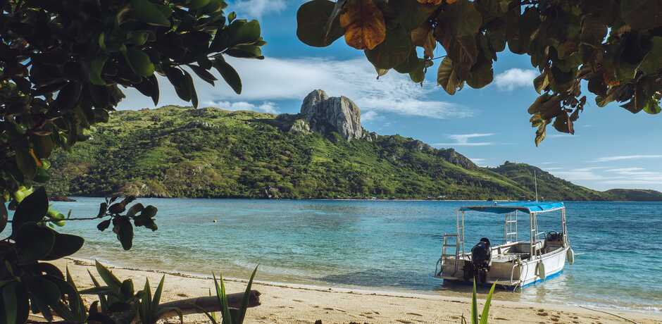 Tropical Fiji beach scene with boat on sand and mountain in background