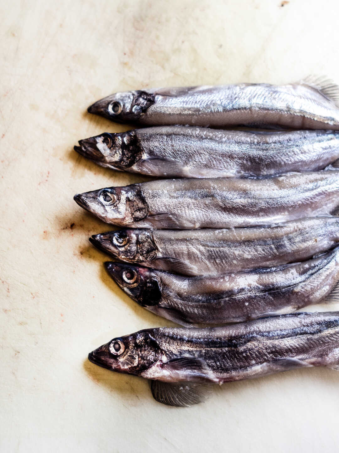 Capelin fish lay side by side on a cutting board. 