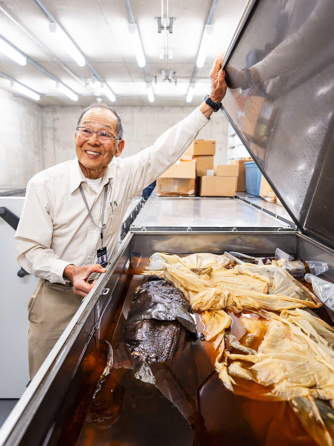 Tomio Iwamoto holding open a large container filled with fish specimens at the Academy. Photo by Gayle Laird
