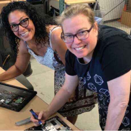 Two smiling teachers working on a technology project together.