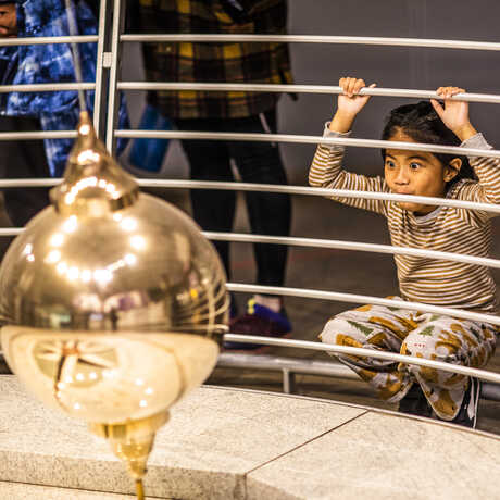 A young girl watches the Foucault pendulum knock down pins at the Academy