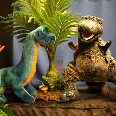 A sauropod and allosaurus hand puppet in a prehistoric puppet show landscape