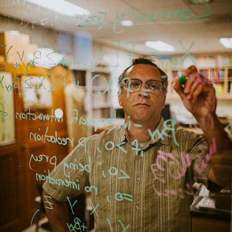 Dr. Peter Roopnarine writes equations on a window in his office