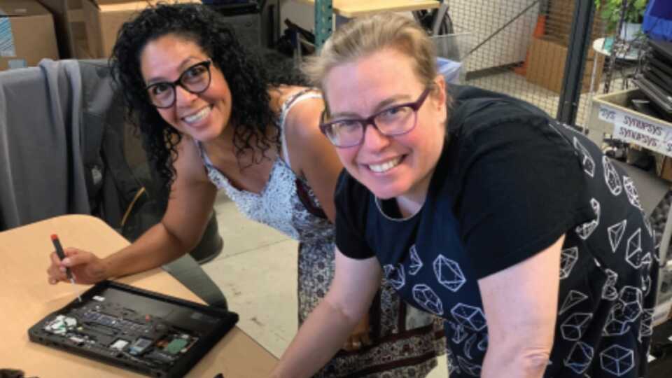 Two smiling teachers working on a technology project together.