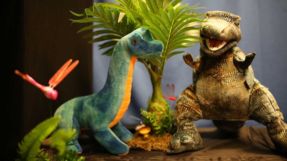 A sauropod and allosaurus hand puppet in a prehistoric puppet show landscape